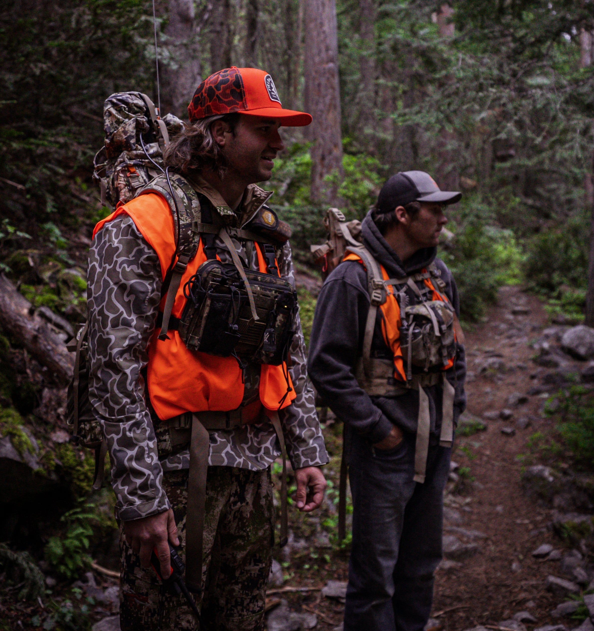 Two hunters on a mountain trail wearing KP chest harnesses loaded with radios and a Garmin handheld